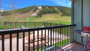 A balcony with a view of a green field and a forested hill.