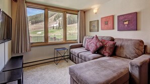 A living room with a large window, a sofa, a small table, and wall-mounted artwork.