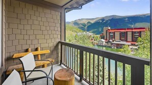 A balcony with a view of mountains and a lake, wooden chairs, and a brick wall. - Comfortable Condo, Outstanding Location - TX414 by RedAwning (Copper Mountain)
