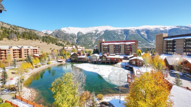 A resort with a clear lake, buildings with large windows, and mountains in the background. - Comfortable Condo, Outstanding Location - TX414 by RedAwning (Copper Mountain)