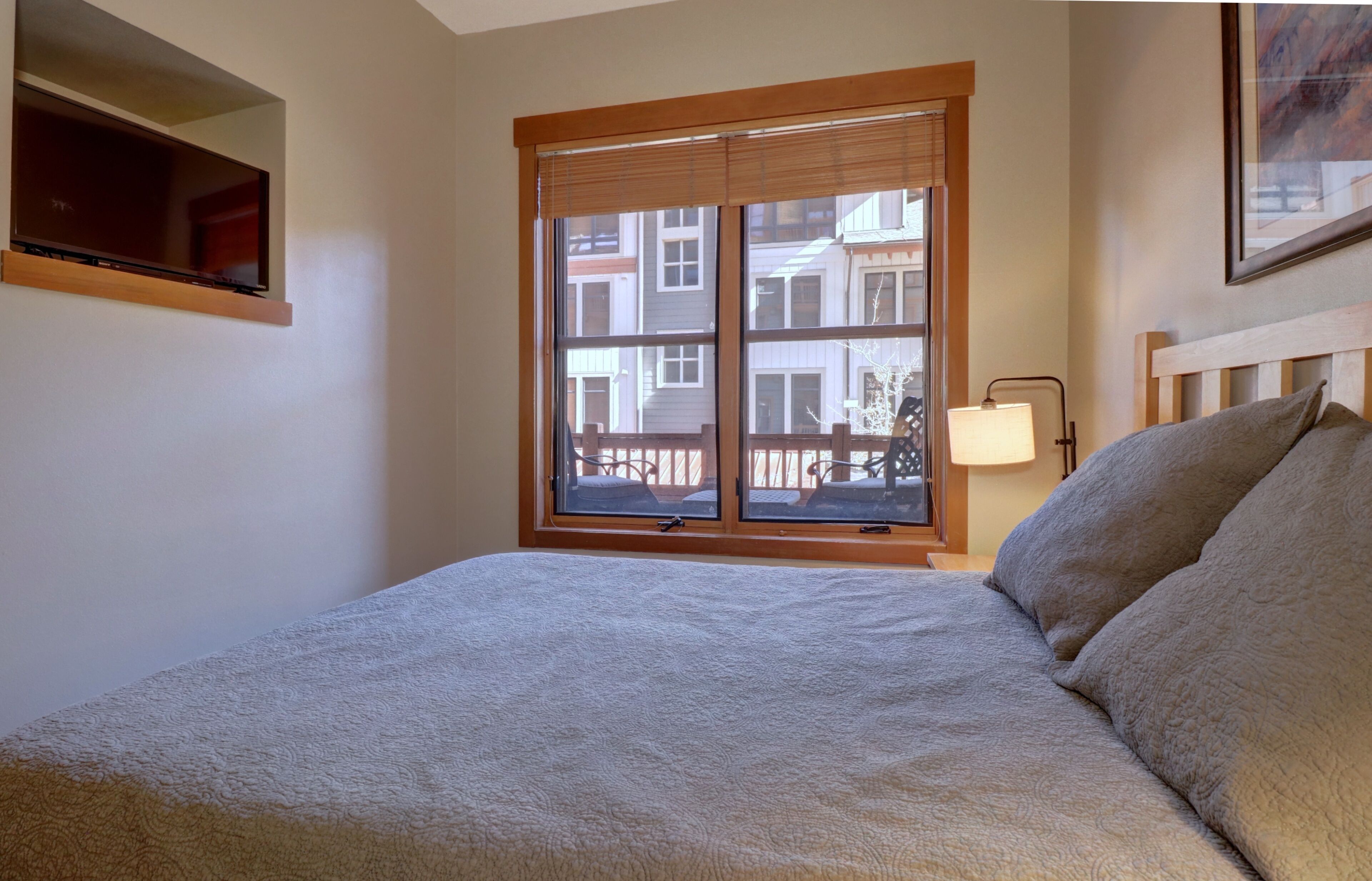 A bedroom with a large window, a bed, a bedside table, and a lamp.