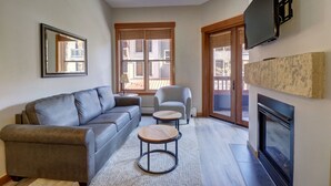 A modern living room with a grey sofa, a round coffee table, a grey armchair, a fireplace, and a large window with blinds. - Best Location On The Mountain, Amazing View - CO204 by RedAwning (Copper Mountain)