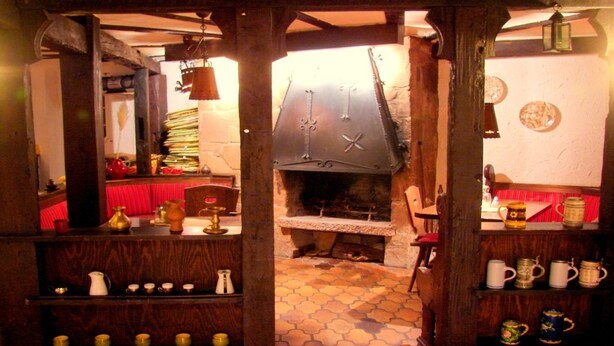 A rustic interior with a stone fireplace, wooden shelves with various items, and a tiled floor. - Hotel Krone (Alsfeld)