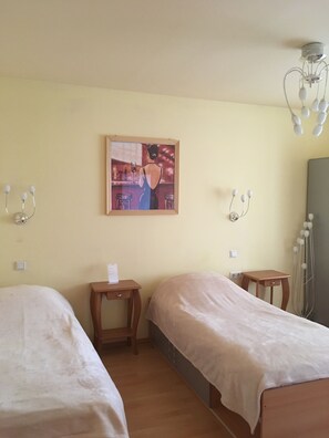Une chambre d’hôtel avec deux lits simples, une petite table en bois, un luminaire fixé au mur et un tableau encadré.