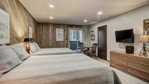Un dormitorio con dos camas, televisor, cómoda y puerta corredera que da a un balcón.