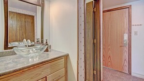 Un baño con lavamanos de vidrio, tocador de madera y espejo con iluminación.
