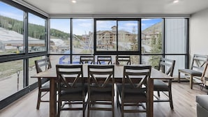 A modern dining area with a large table and chairs, large windows offering a view of a ski resort and buildings. - Amazing Location - Steps to American Eagle Lift - CJ202 by RedAwning (Copper Mountain)