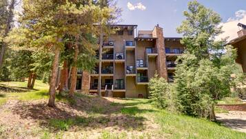 A multi-story building with balconies, surrounded by trees and a grassy area.