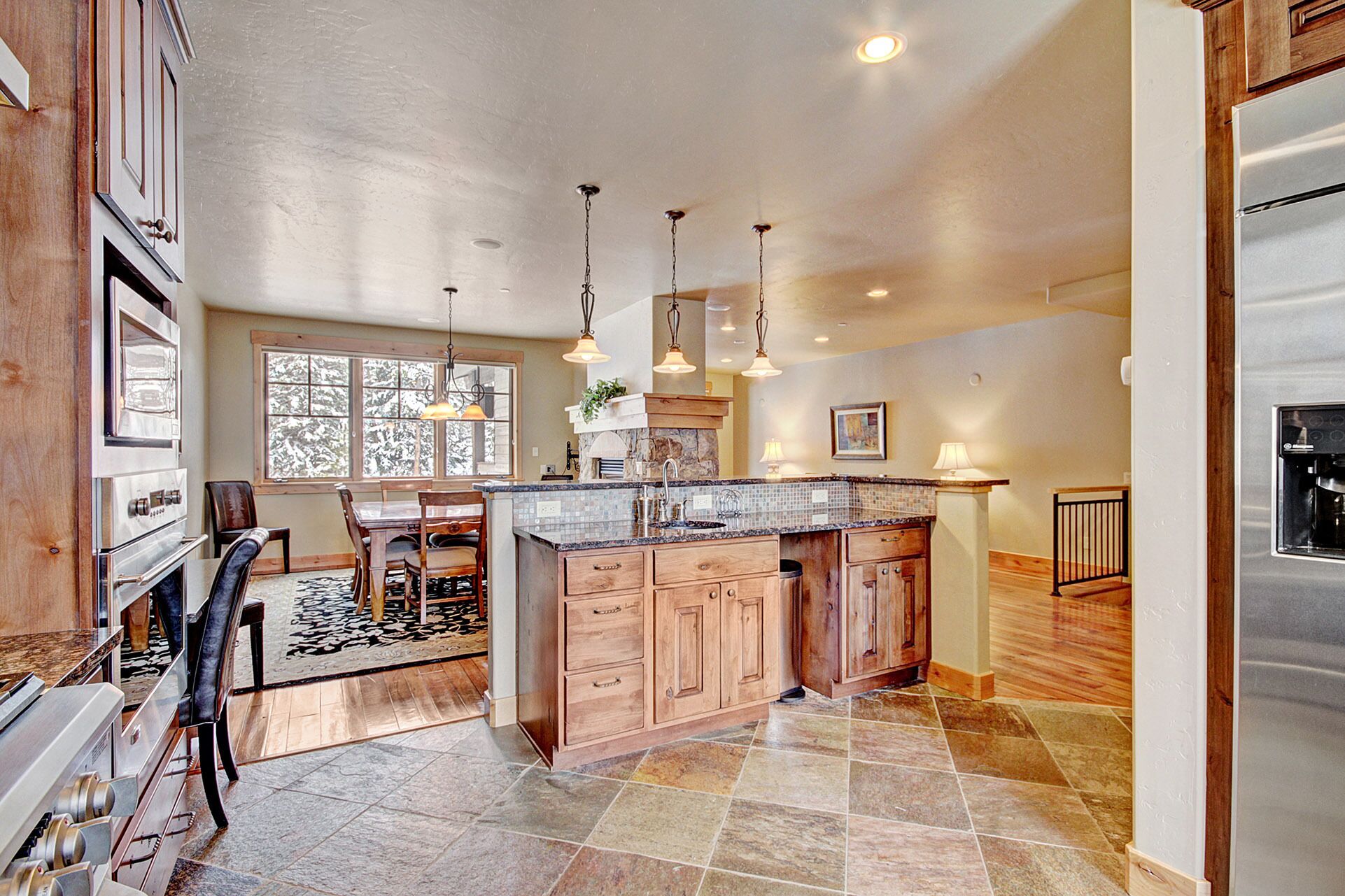 A spacious kitchen with a large island, wooden cabinets, and a stone tile floor.