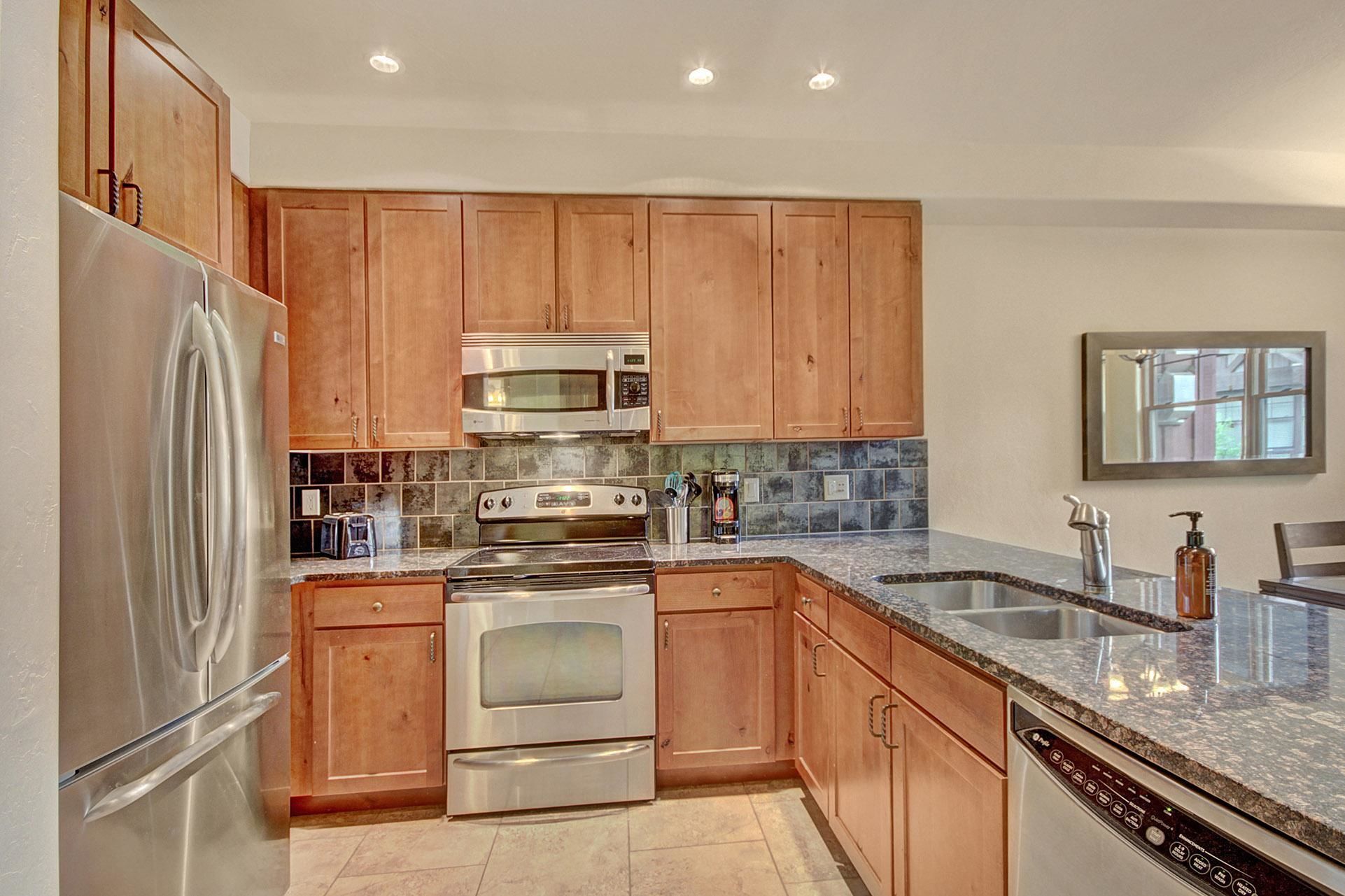 A modern kitchen with wooden cabinets, stainless steel appliances, a granite countertop, and a built-in dishwasher.