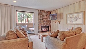 A cozy living room with a stone fireplace, comfortable sofas, a television, and a large window with curtains. - CM116S and 117H Copper Mtn Inn by RedAwning (Copper Mountain)