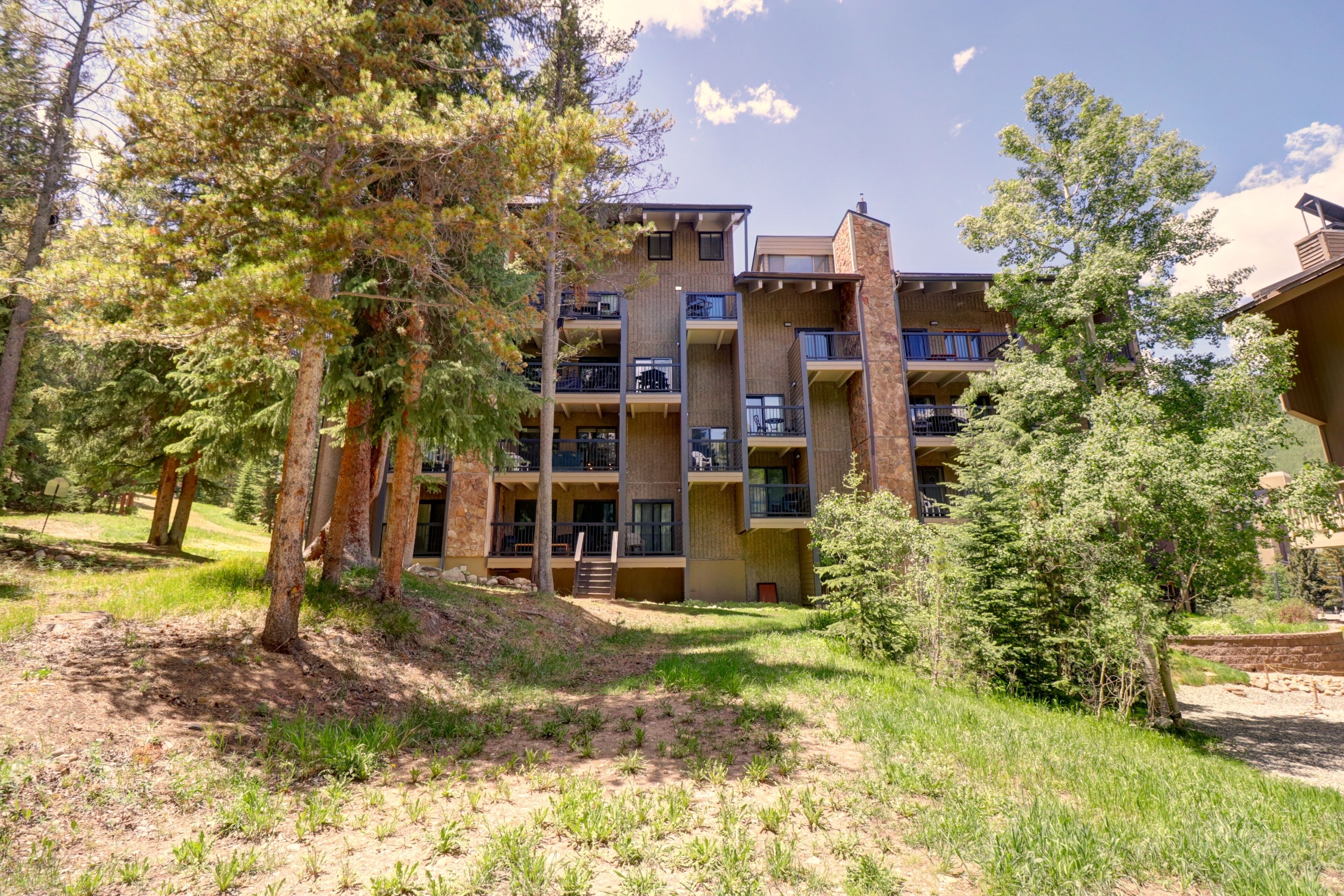 A multi-story building with balconies, surrounded by trees and a grassy area.