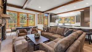 A spacious living area with a large sofa, a coffee table, and a fireplace. There are multiple windows providing natural light and views of the outdoors. - Beautiful Executive Ski-In Ski-Out Rooftop Hot tub - LR962 by RedAwning (Copper Mountain)