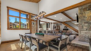 A spacious living area with a wooden dining table and chairs, a stone fireplace, and a view of the outside. - Beautiful Executive Ski-In Ski-Out Rooftop Hot tub - LR962 by RedAwning (Copper Mountain)
