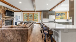A modern kitchen with a stone fireplace, a large island with bar stools, and a view of the outdoors. - Beautiful Executive Ski-In Ski-Out Rooftop Hot tub - LR962 by RedAwning (Copper Mountain)