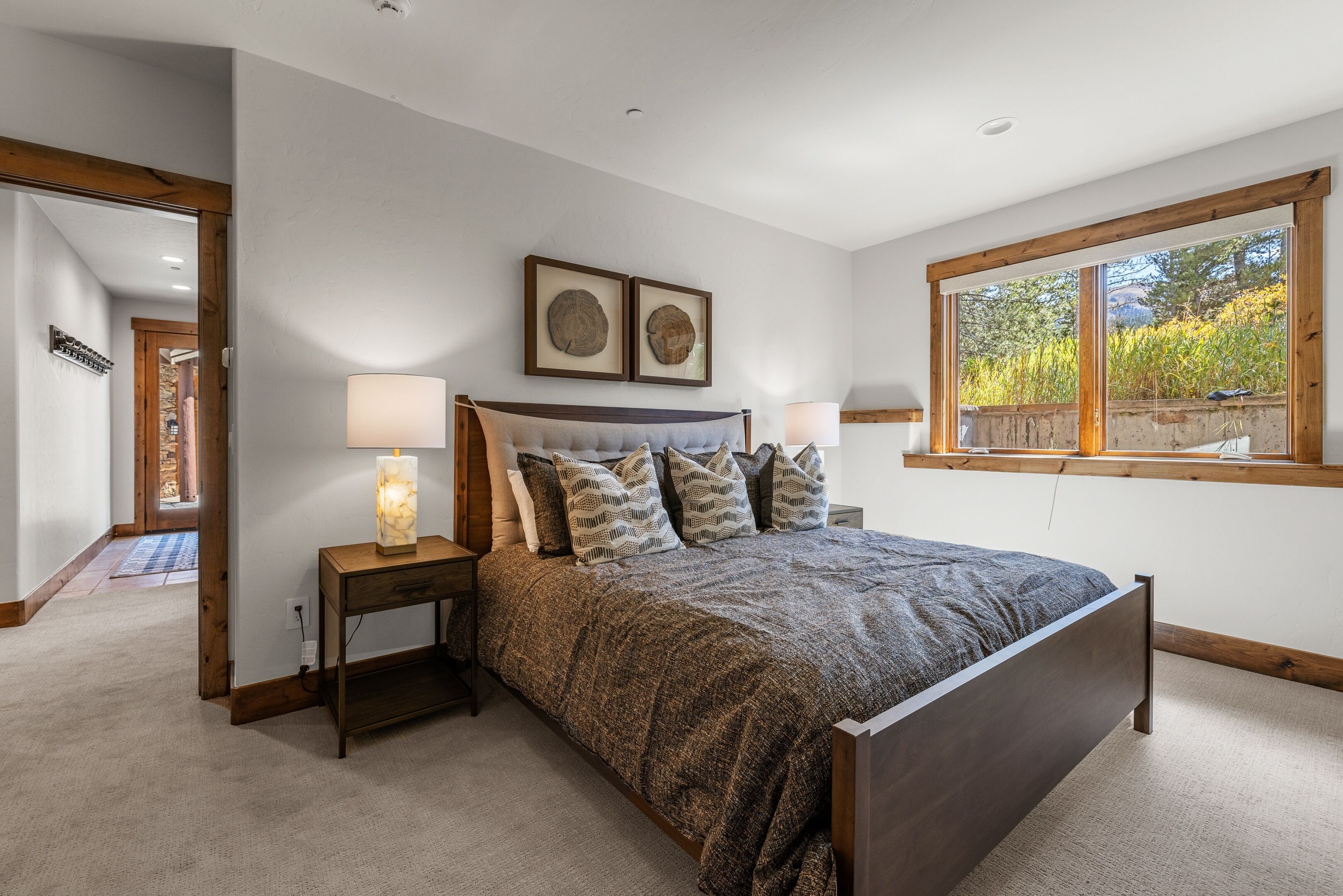 Une chambre à coucher avec un grand lit, deux lampes de chevet, une tête de lit en bois et deux tableaux encadrés accrochés au mur.