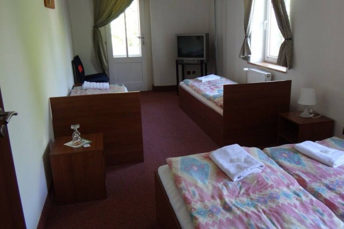 A hotel room with two beds, a TV, a small table, and a window with curtains.