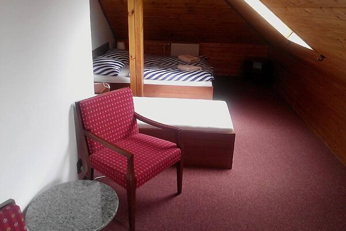 A small attic room with a sloped ceiling, a single red chair, a small round table, and two beds with striped bedding.