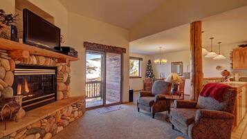 A cozy living room with a stone fireplace, comfortable seating, and a large TV.