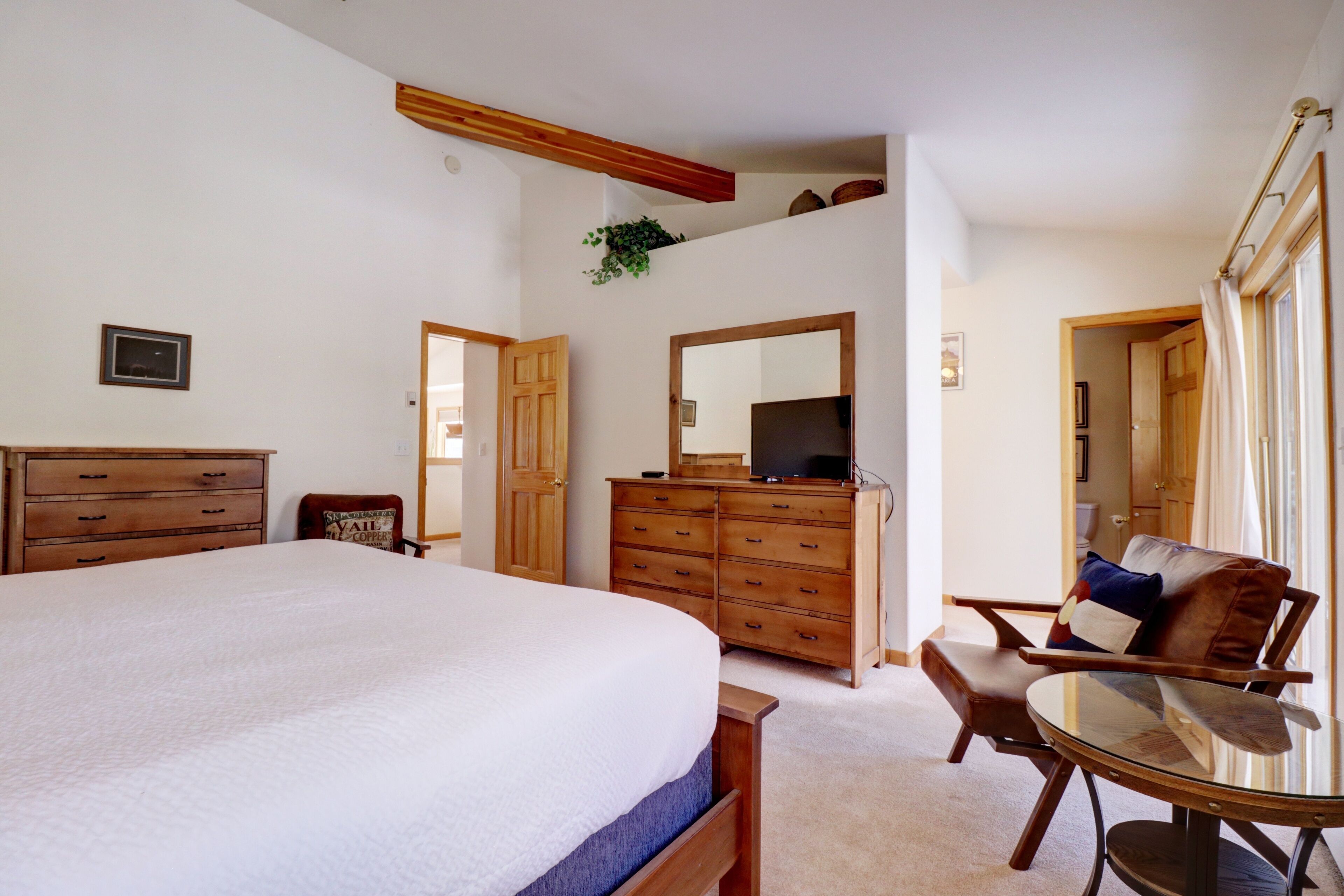 A bedroom with a large bed, wooden dresser, a TV, and a seating area with a table and chairs.