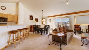 Una sala de estar con sofá, mesa de centro y sillas, un comedor con mesa y sillas, y una cocina con microondas y armarios de madera.