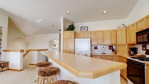 Una cocina moderna con armarios de madera, una isla grande con taburetes, un refrigerador, estufa y microondas.