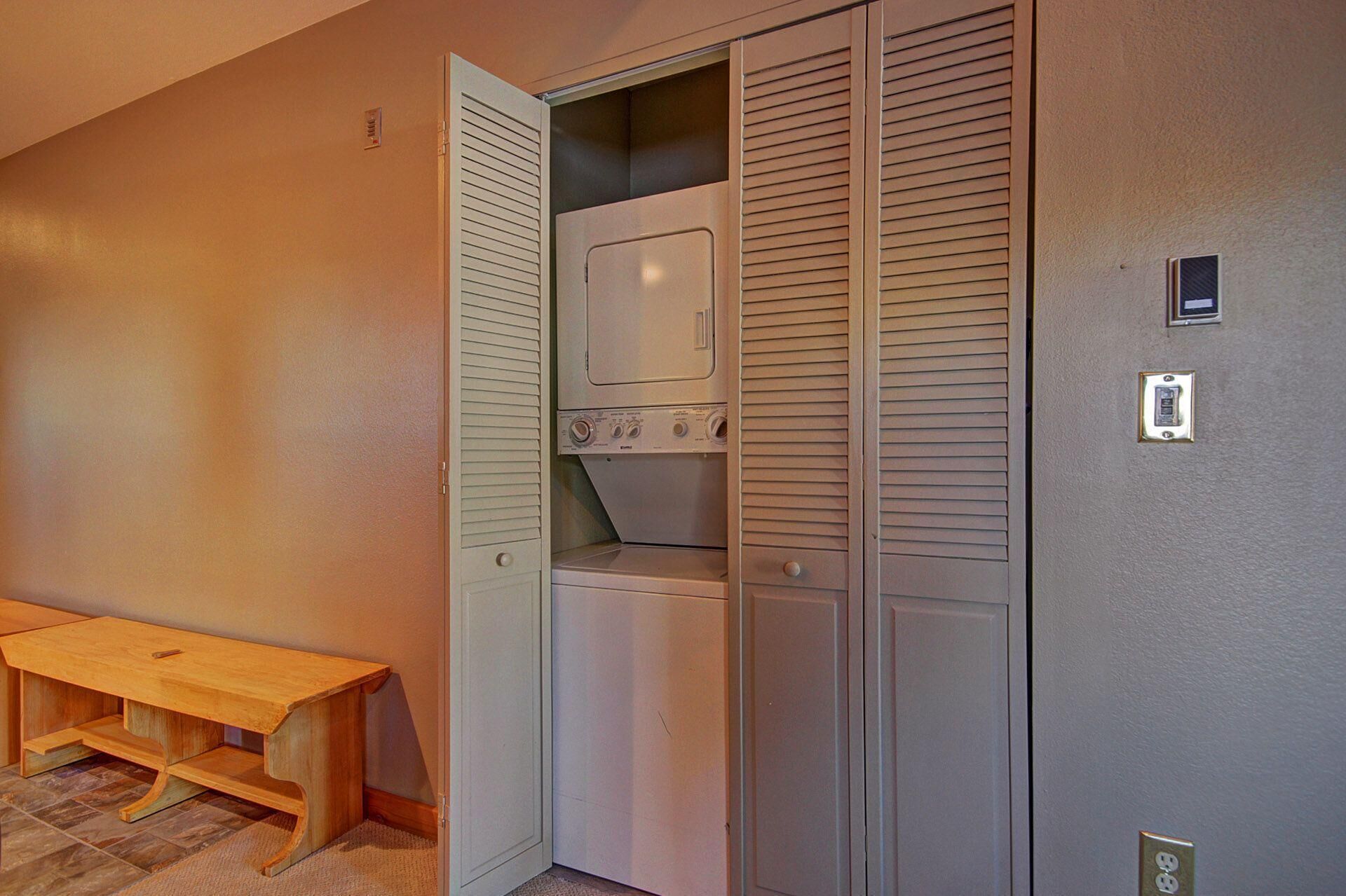 A laundry room with a washing machine and dryer, a bench, and a utility wall with electrical outlets.
