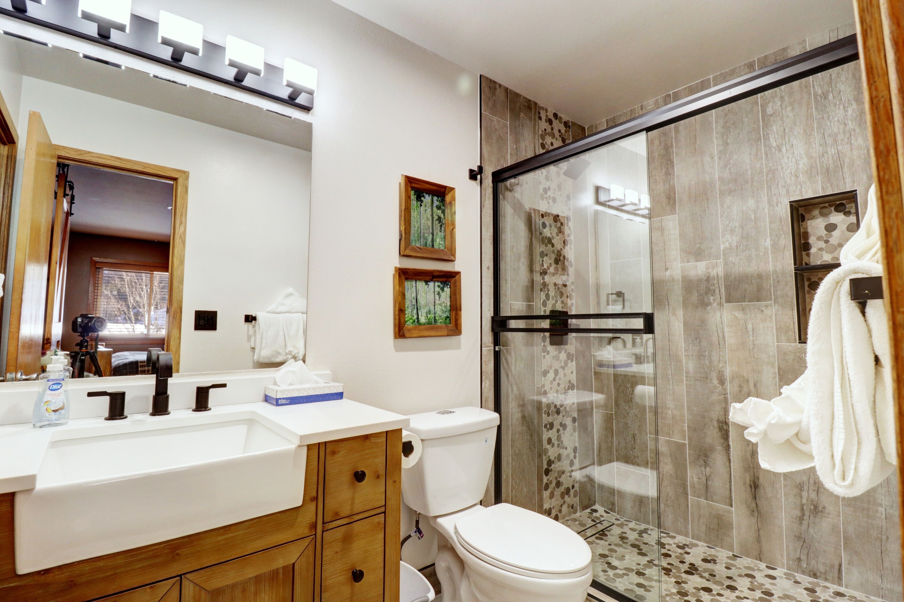A modern bathroom with a large mirror, a sink, a toilet, and a glass-enclosed shower.