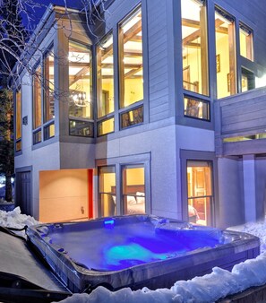 Una casa de dos pisos con amplios ventanales y un jacuzzi visible al frente.