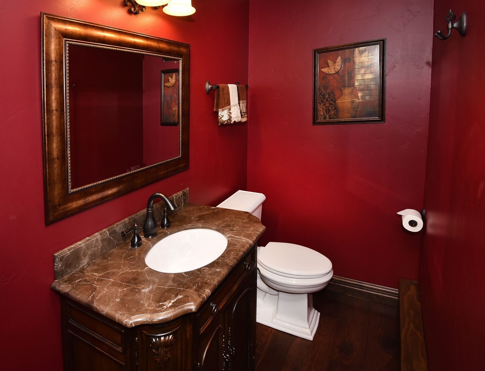 A bathroom with a marble sink, a white toilet, a large mirror, and a framed artwork on the wall.