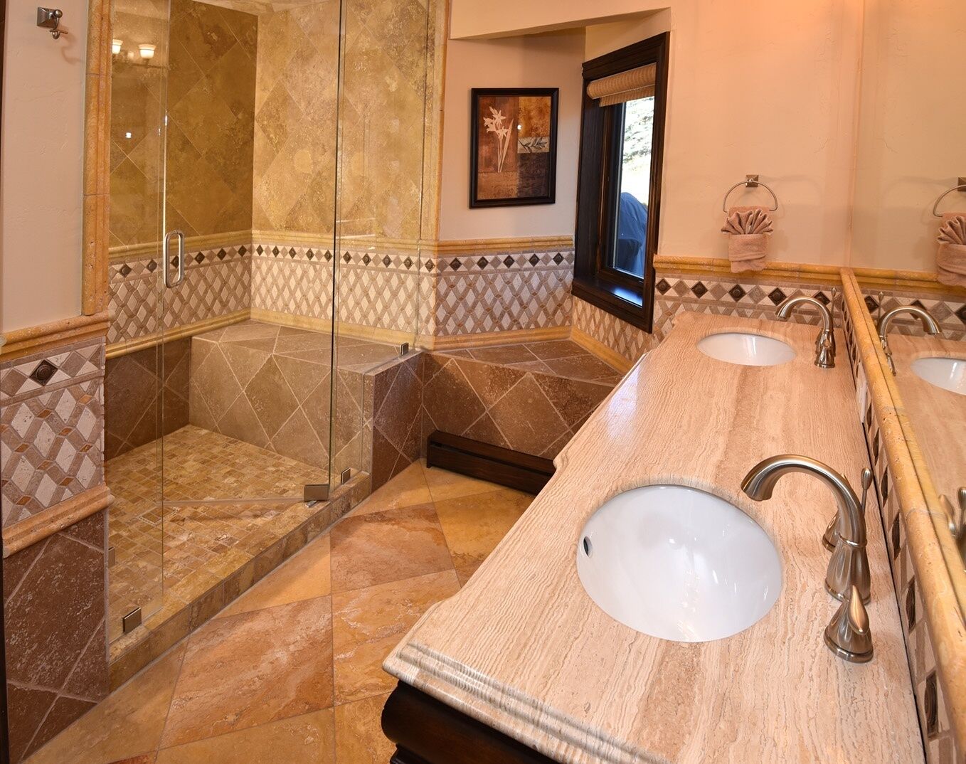 Un baño con ducha de vidrio, dos lavamanos con grifos modernos y un borde decorativo de azulejos en la pared.