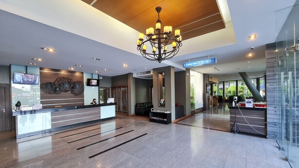 A modern hotel lobby with a reception desk, a chandelier, a TV screen, and a sign pointing to the garden wing.