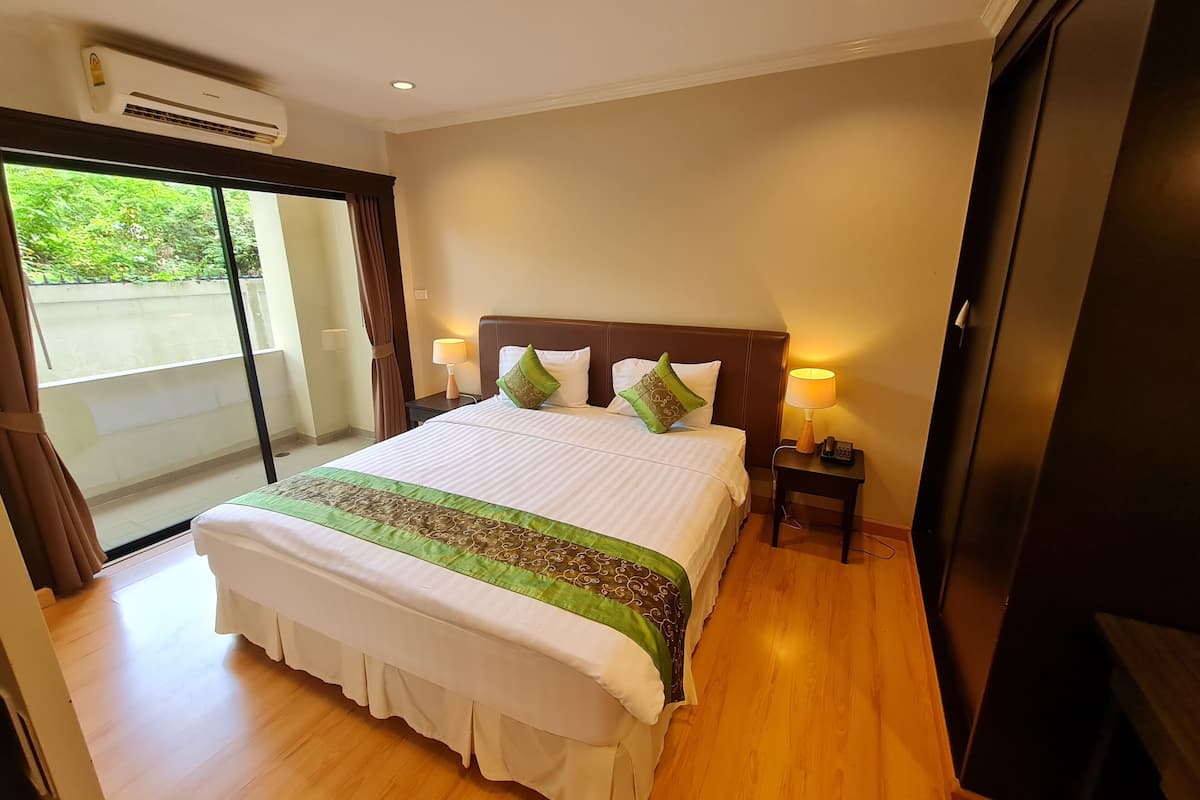 Une chambre d’hôtel avec un grand lit, deux tables de chevet avec des lampes, un appareil de climatisation et une vue sur l’extérieur, accessible par une porte coulissante.