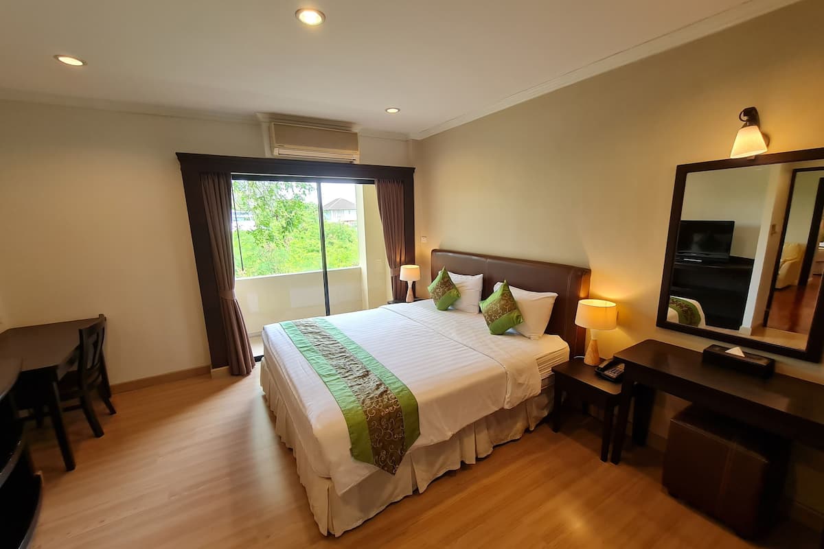 Une chambre d’hôtel avec un grand lit, un bureau, une chaise, un miroir et une fenêtre avec des rideaux.