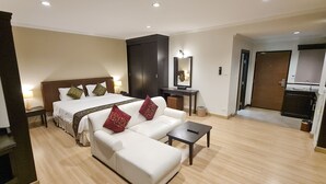 A hotel room with a bed, a sofa, a small table, a desk, a mirror, a wardrobe, and a kitchenette.