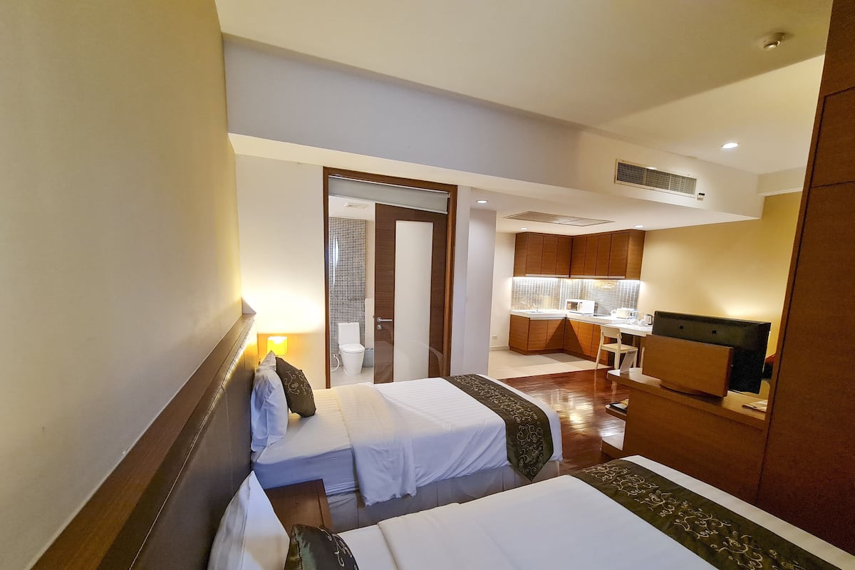 Une chambre d’hôtel avec deux lits, une petite kitchenette et une salle de bain visible par une porte ouverte.