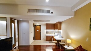 A modern living room with a flat-screen TV, a sofa, and a coffee table. There is a kitchen area with a dining table and chairs, and a small kitchenette with a microwave and toaster.