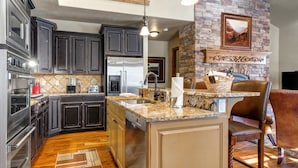 A modern kitchen with dark cabinets, a granite countertop, and a stone fireplace. - Stillwater Shores 1273 5 Bedroom Townhouse by RedAwning (Heber City)