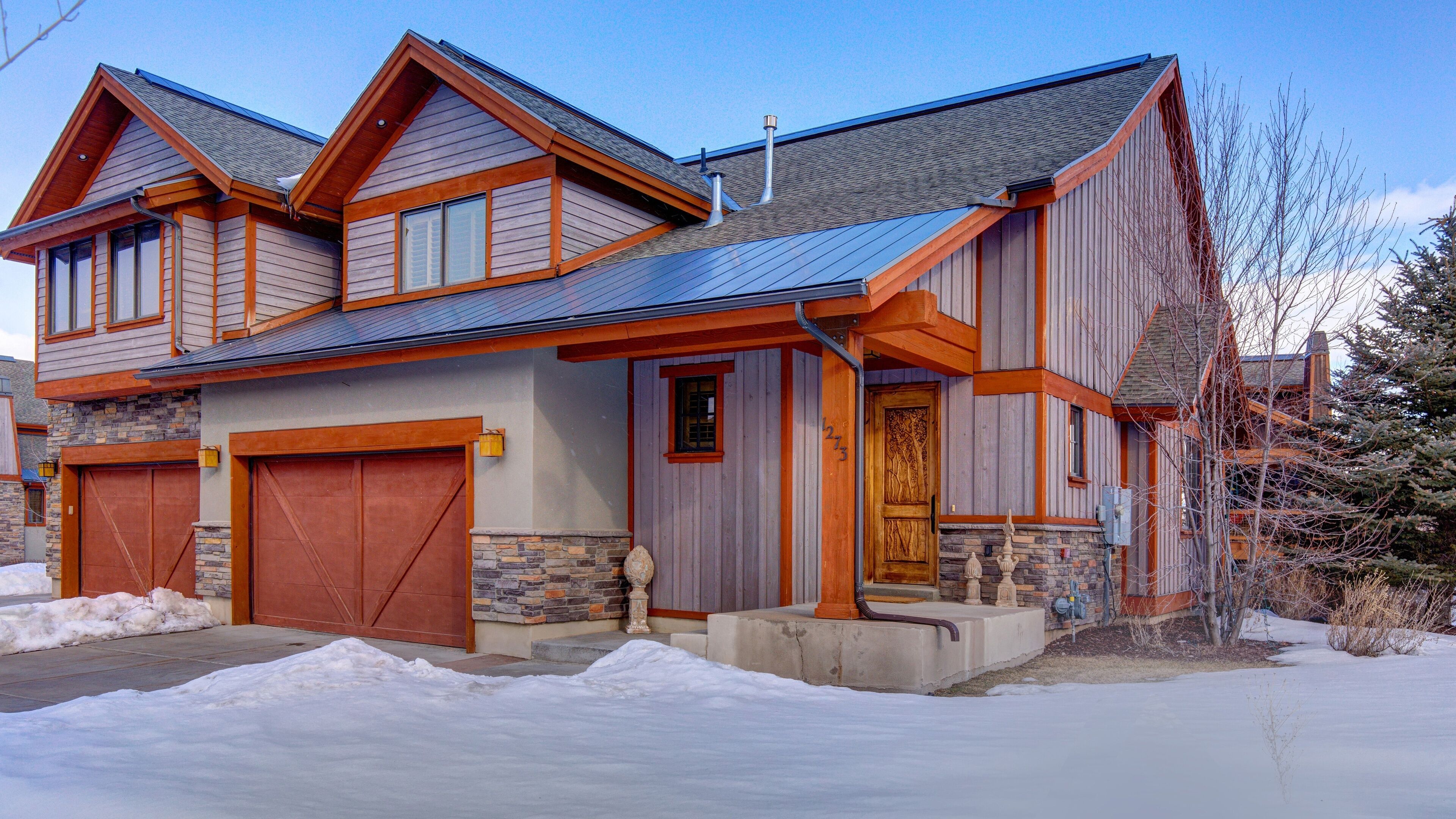 A two-story house with a stone foundation, wooden siding, and a metal roof.