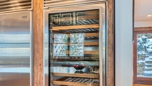 Een moderne keuken met een roestvrijstalen koelkast, houten planken en een glazen deur met uitzicht op een besneeerd landschap.