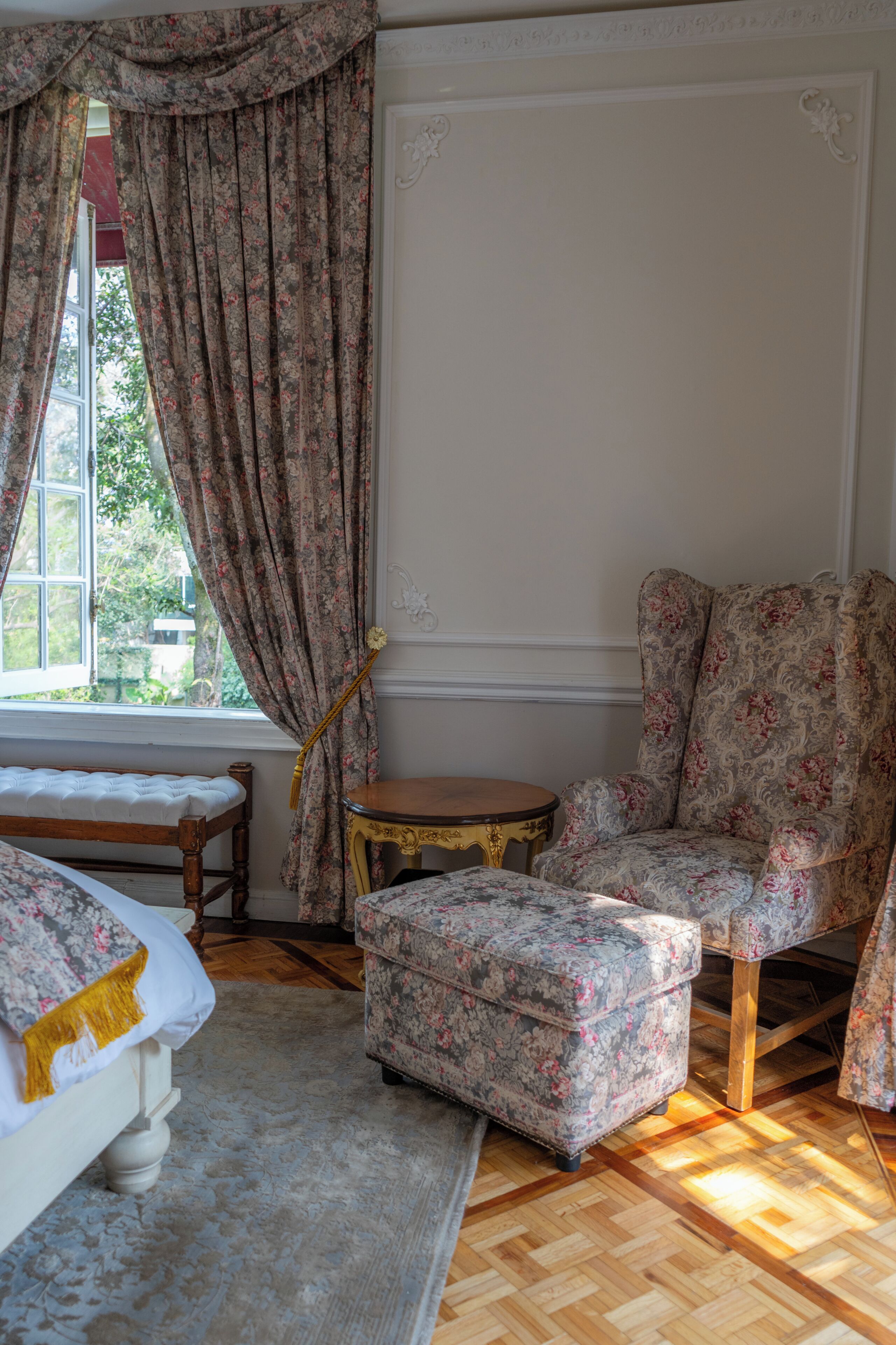 Une pièce comprenant un lit, une chaise, une petite table et une fenêtre avec des rideaux.