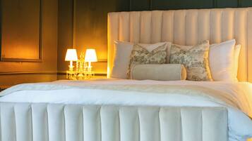 A large bed with a tufted headboard, a bedside table with two lamps, and a patterned rug.