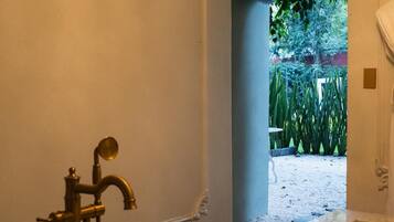 Een badkamer met een marmeren bad, een gouden kraan en uitzicht op een tuin door een bogenpoort.
