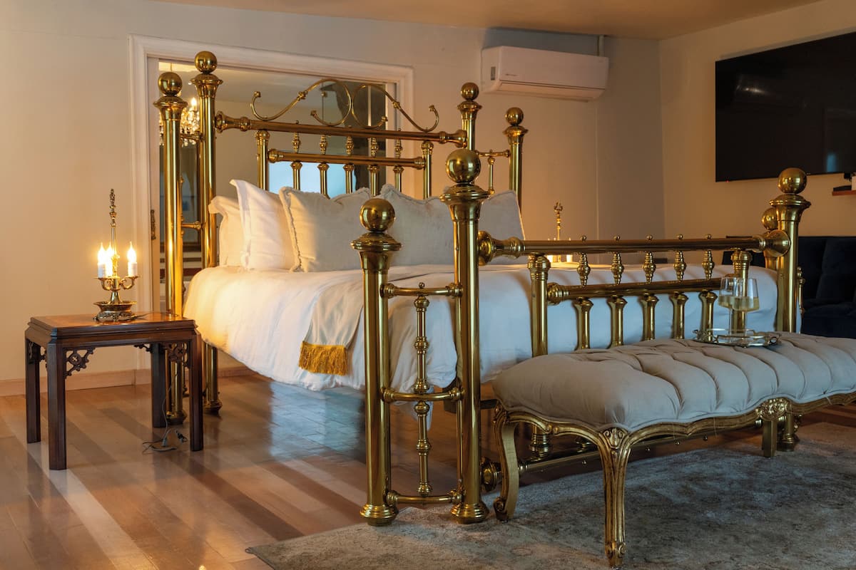 A four-poster bed with a canopy, a bedside table with a lamp, and a large flat-screen TV mounted on the wall.