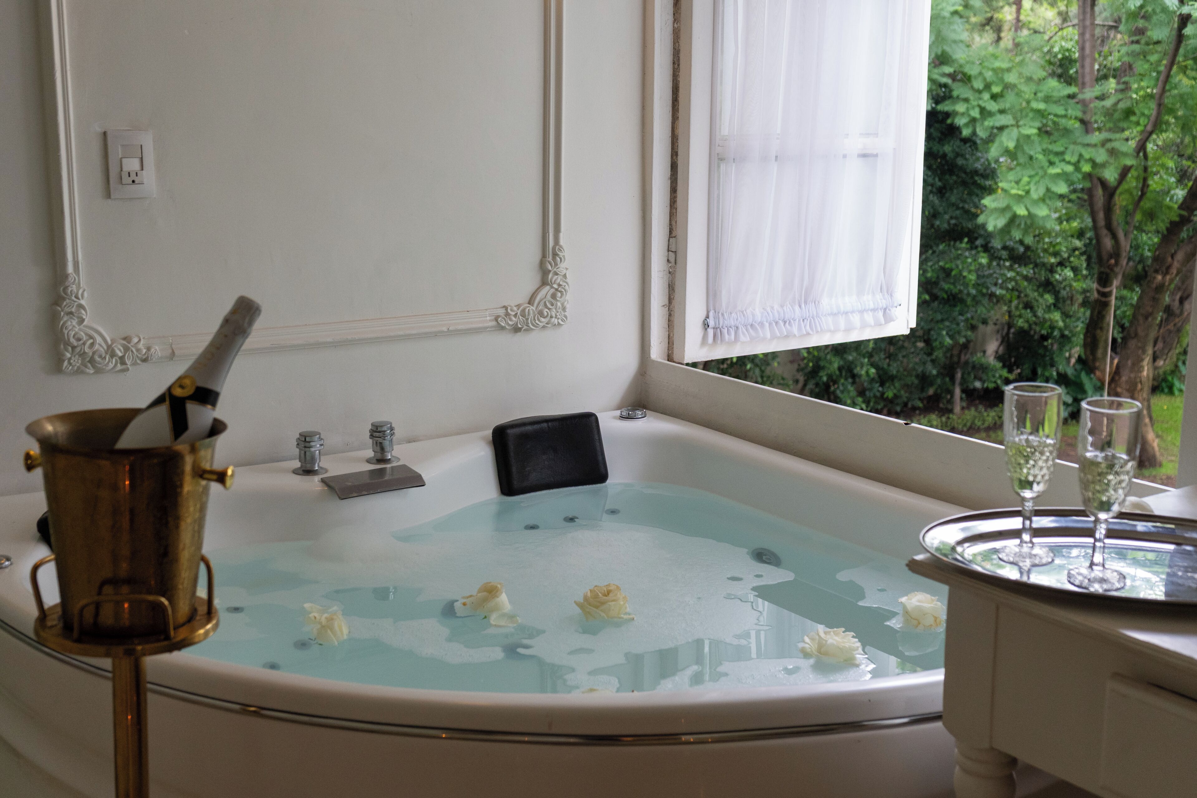 A bathtub with a champagne bottle, glasses, and flowers.