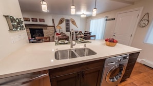 A kitchen with a double sink, a built-in washing machine, pendant lighting, and a dining area with a table set for two.