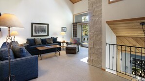 A spacious living room with a high ceiling, a stone wall, and a view of the outdoors. - 188 Ridgepoint 3 Bedroom Townhouse by RedAwning (Avon)