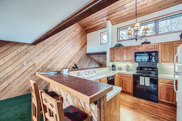 Une cuisine dotée de meubles en bois, d’une cuisinière noire et d’un coin repas avec une table et des chaises en bois.