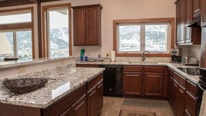 A kitchen with wooden cabinets, granite countertops, a dishwasher, and a window with a mountain view.
