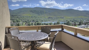 A balcony with a round table and chairs, overlooking a scenic view of mountains and a lake.